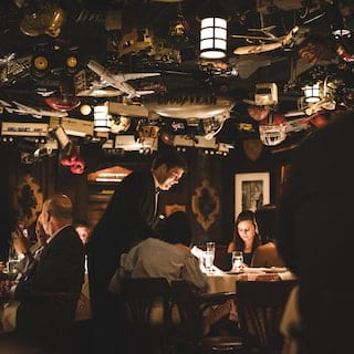 Guests at tables in a dark-lit restaurant with an eclectic collection of ceiling ornaments