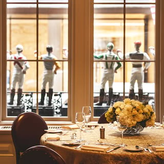 A formal dinner table beside a large window lined with jockey figurines
