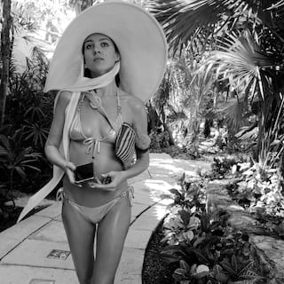 Lady in a gold swimsuit and large sunhat strolling along a garden path