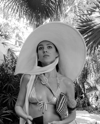 Mujer en traje de baño con un sombrero de gran tamaño paseando por el sendero de un jardín tropical