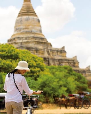 Lady wheeling a bicycle towards an ancient pagoda