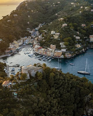 Aerial view of Portofino harbour in an orange sunset with sailing boats approaching