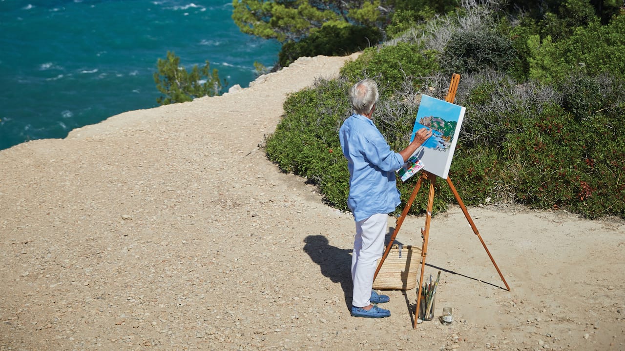 Man painting a canvas on an easel on the beach beside the blue sea