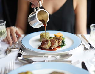 a steward is pouring a gravy over a guest's dish